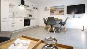 Eine moderne Küche mit weißen Schränken, einem eingebauten Backofen und einer Mikrowelle. Ein Essbereich mit Tisch und Stühlen, sowie ein an der Wand befestigter Flachbildfernseher.