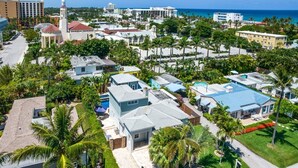 An aerial view of a coastal residential area with houses, a church, and a beach in the background.