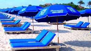 A beach with rows of blue lounge chairs and umbrellas, some with 'Oceanside Beach Service' branding.