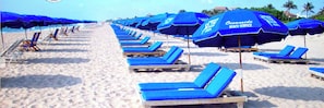 Una playa con filas de sillas azules y sombrillas, algunas con el logotipo de 'Oceanside Beach Service'.