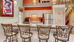 A kitchen with a central island, bar stools, and a hanging light fixture. - Timbernest Condo - 2 BDR Walk to Downtown & Lift! (Breckenridge)