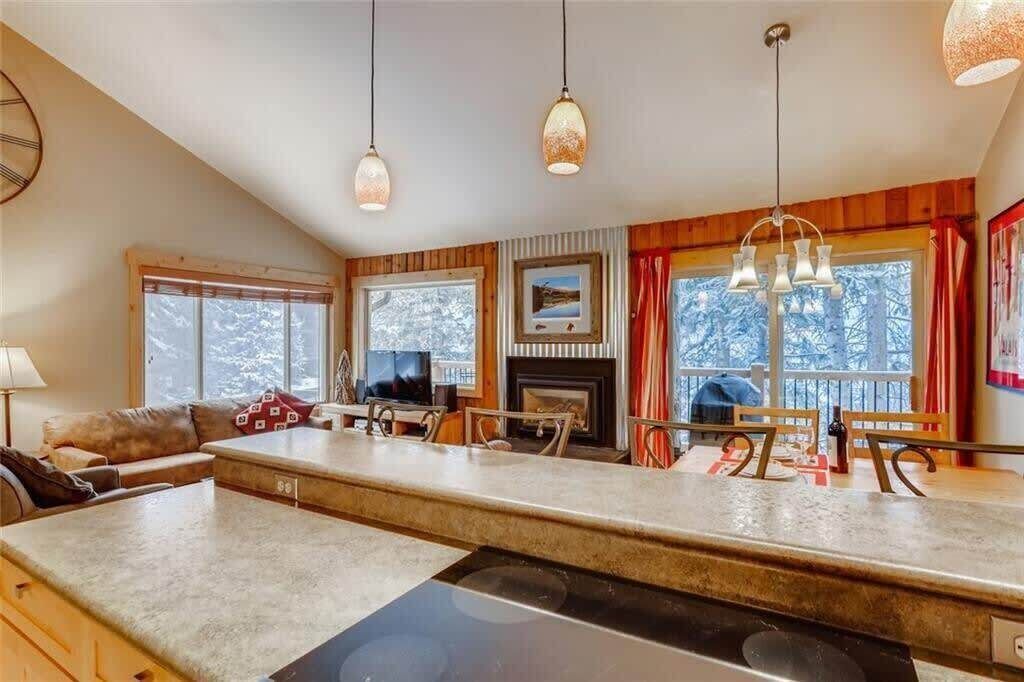 Una cocina moderna con una isla central, detalles de madera y grandes ventanales con vistas a árboles.