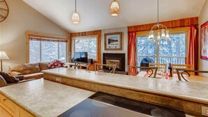 A modern kitchen with a central island, wooden accents, and large windows offering views of trees. - Timbernest Condo - 2 BDR Walk to Downtown & Lift! (Breckenridge)