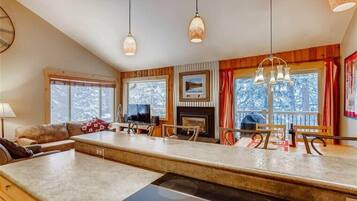 Una cocina moderna con una isla central, detalles de madera y grandes ventanales con vistas a árboles.