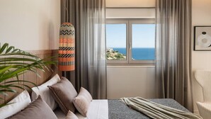 Een hotelkamer met een bed, een raam met uitzicht op zee, een decoratief object en een plant.