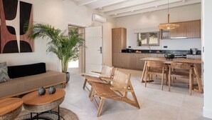 Een moderne woonkamer met een bank, stoelen, een eettafel en een keukenhoek met houten kasten en een hanglamp.