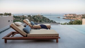 Een terras op het dak met twee loungestoelen, een helder uitzicht op de zee en een rotsachtig landschap op de achtergrond.