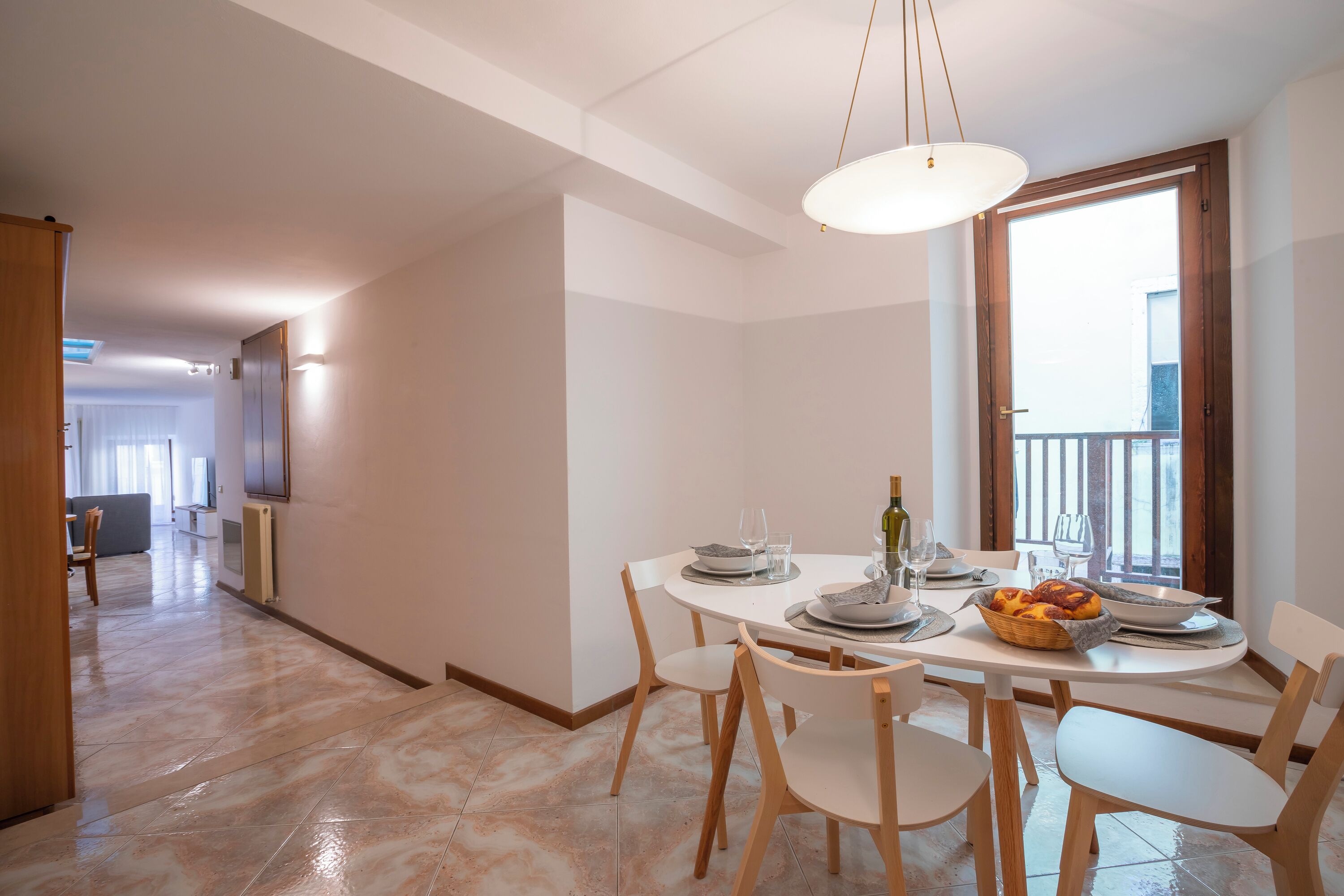 Un coin repas avec une table dressée pour quatre personnes, un lustre et une vue sur l’extérieur par une fenêtre.