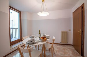 A dining area with a round table, chairs, a chandelier, a window, and a radiator.