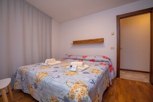A bedroom with a bed, a small table, a wooden shelf, and a door.