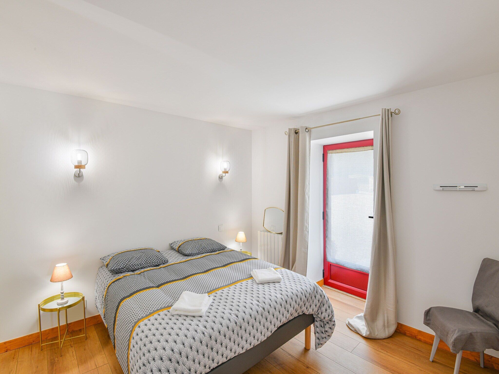A modern bedroom with a bed, bedside lamps, a chair, and a window with curtains.