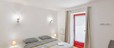 A modern bedroom with a bed, bedside lamps, a chair, and a window with curtains.