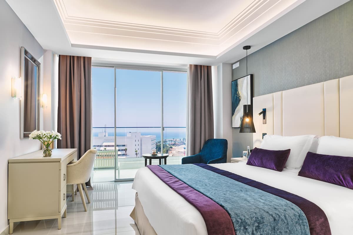A modern hotel room with a large bed, a desk, and a view of the city.