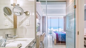 A modern hotel room with a bathroom featuring a large mirror, a sink, and a vanity. The room has a balcony with a view of the sea. - Amanti, MadeForTwo Hotels – Ayia Napa (Ayia Napa)