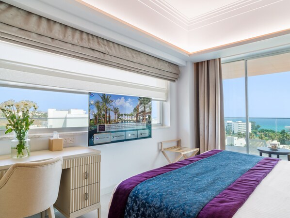 A hotel room with a bed, a desk with a computer, a window with a view of the city, and a view of the ocean. - Amanti, MadeForTwo Hotels – Ayia Napa (Ayia Napa)