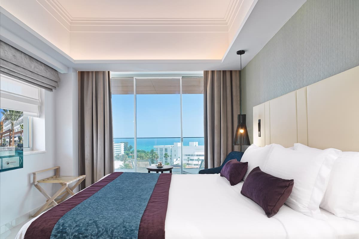 A hotel room with a large bed, a view of the ocean, and a balcony.