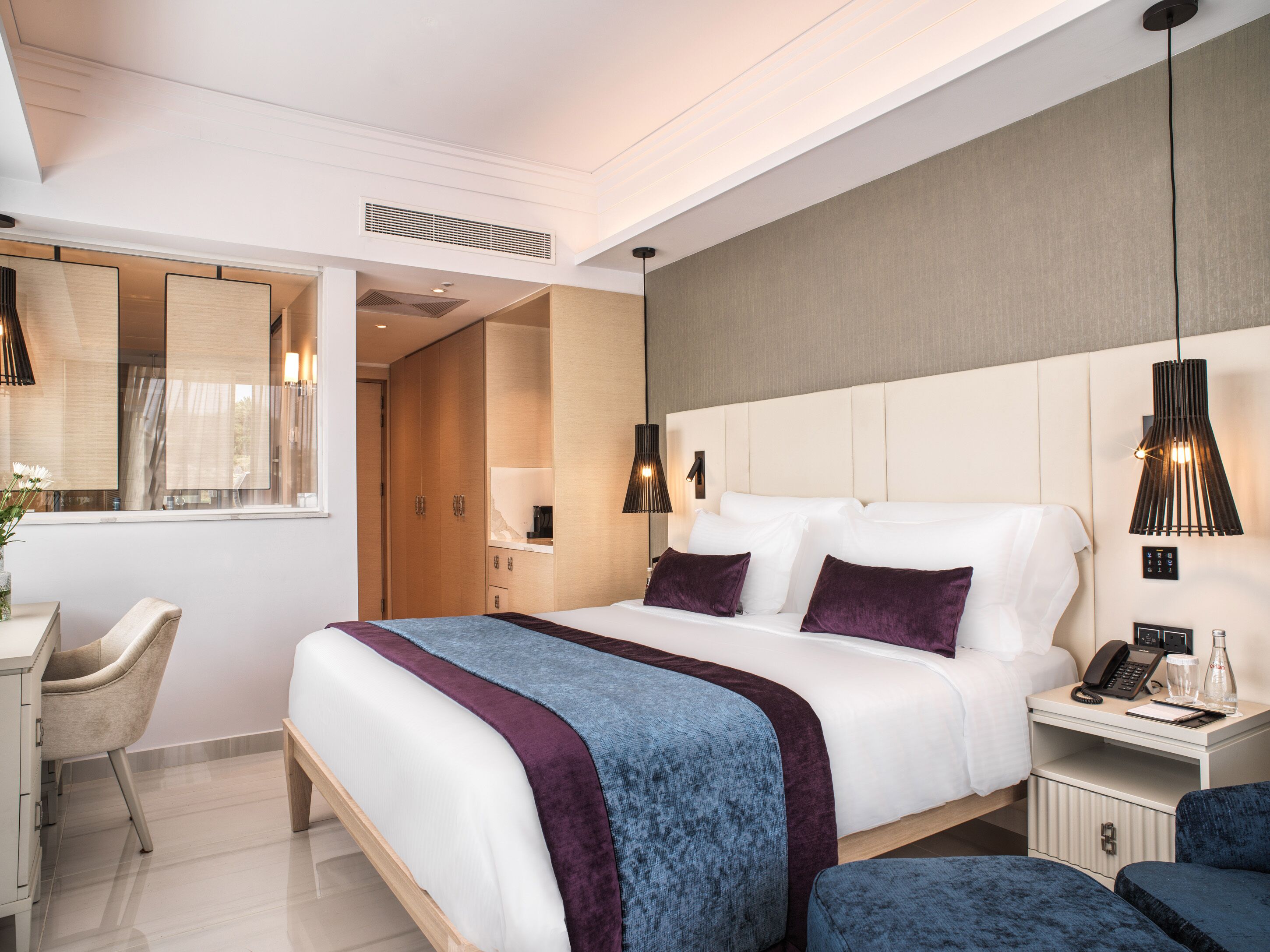 A modern hotel room with a large bed, bedside tables, a desk, and a chair.