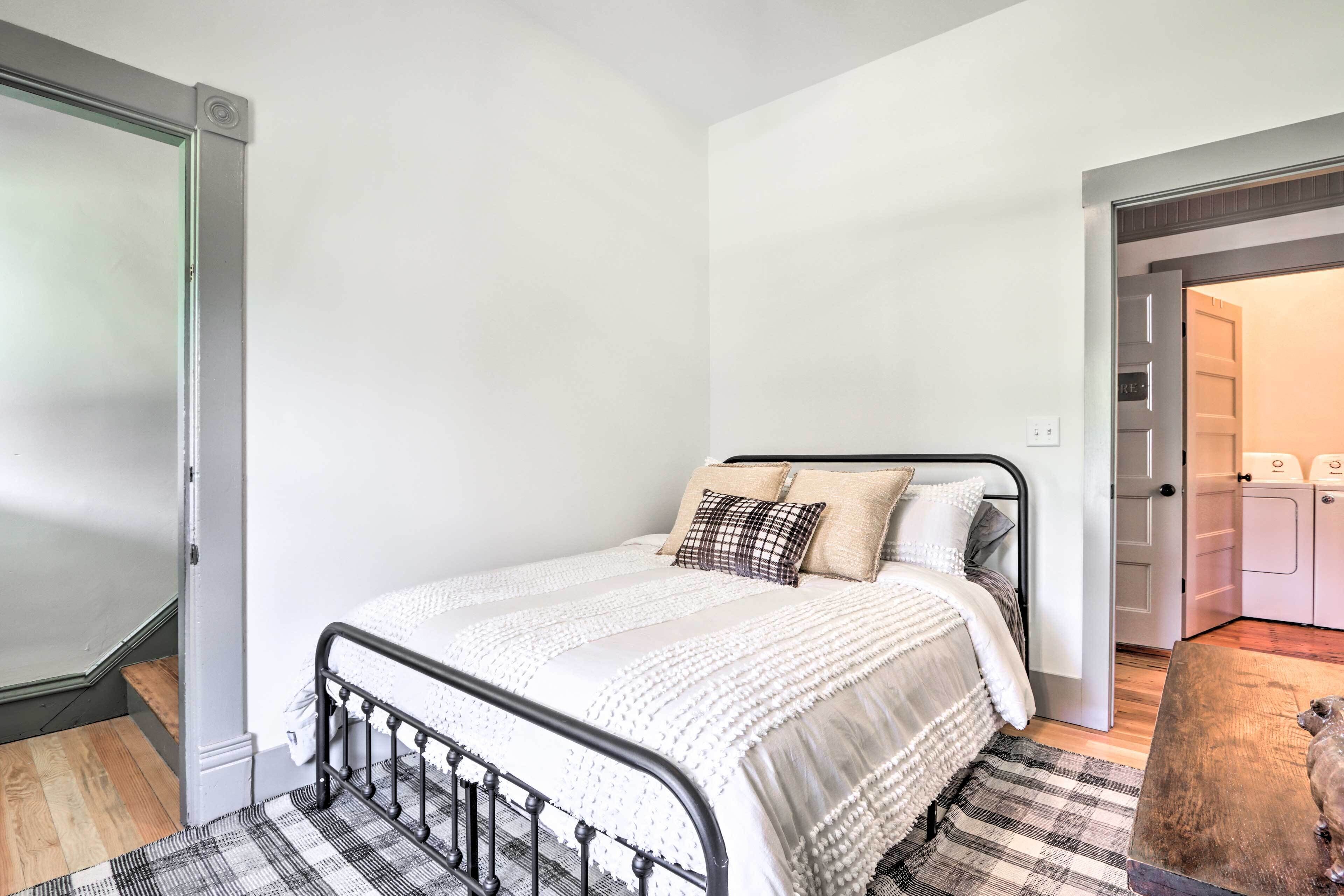 Una camera da letto con un letto, un pavimento in legno, un tappeto a scacchi e una porta che dà su un locale lavanderia.
