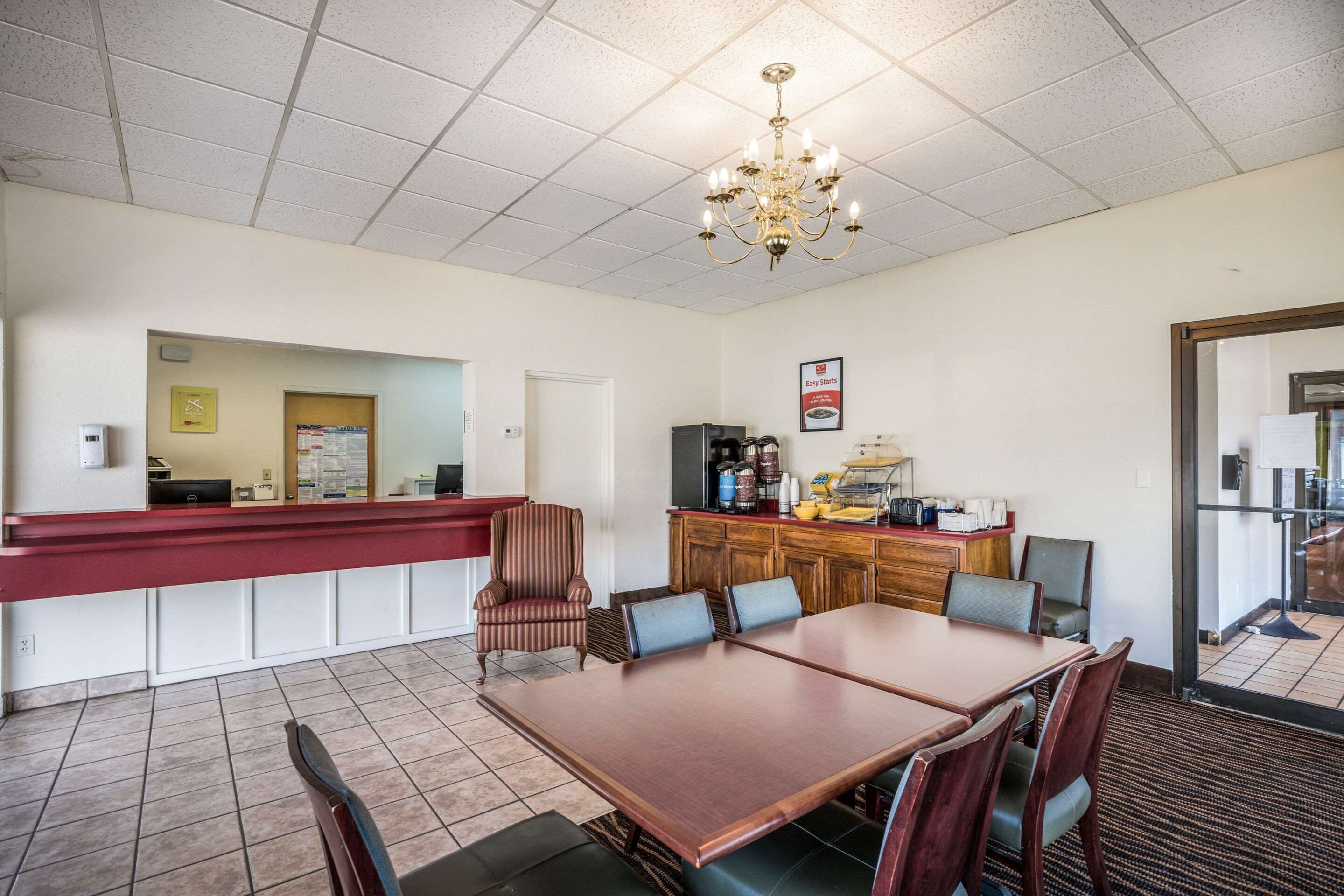 A hotel room with a dining area, a reception desk, a kitchenette, and a chandelier.
