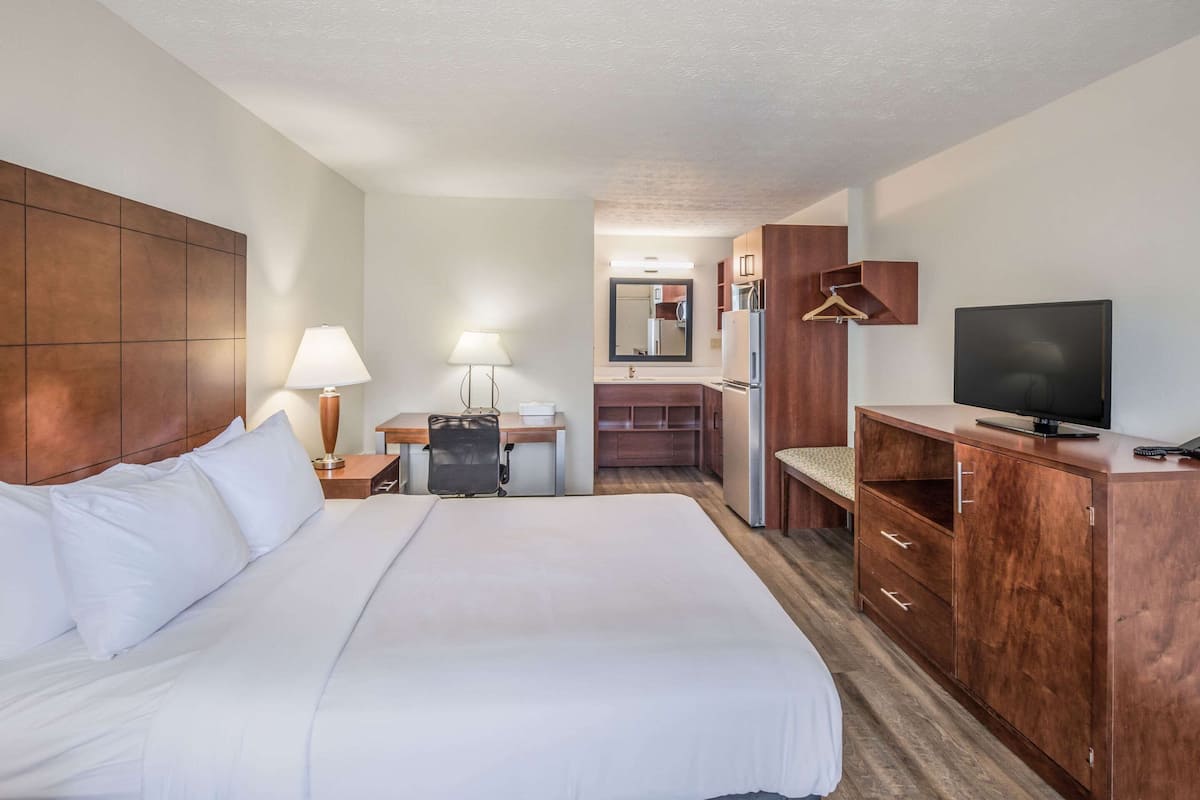A hotel room with a large bed, a desk with a chair, a television, and a wardrobe.