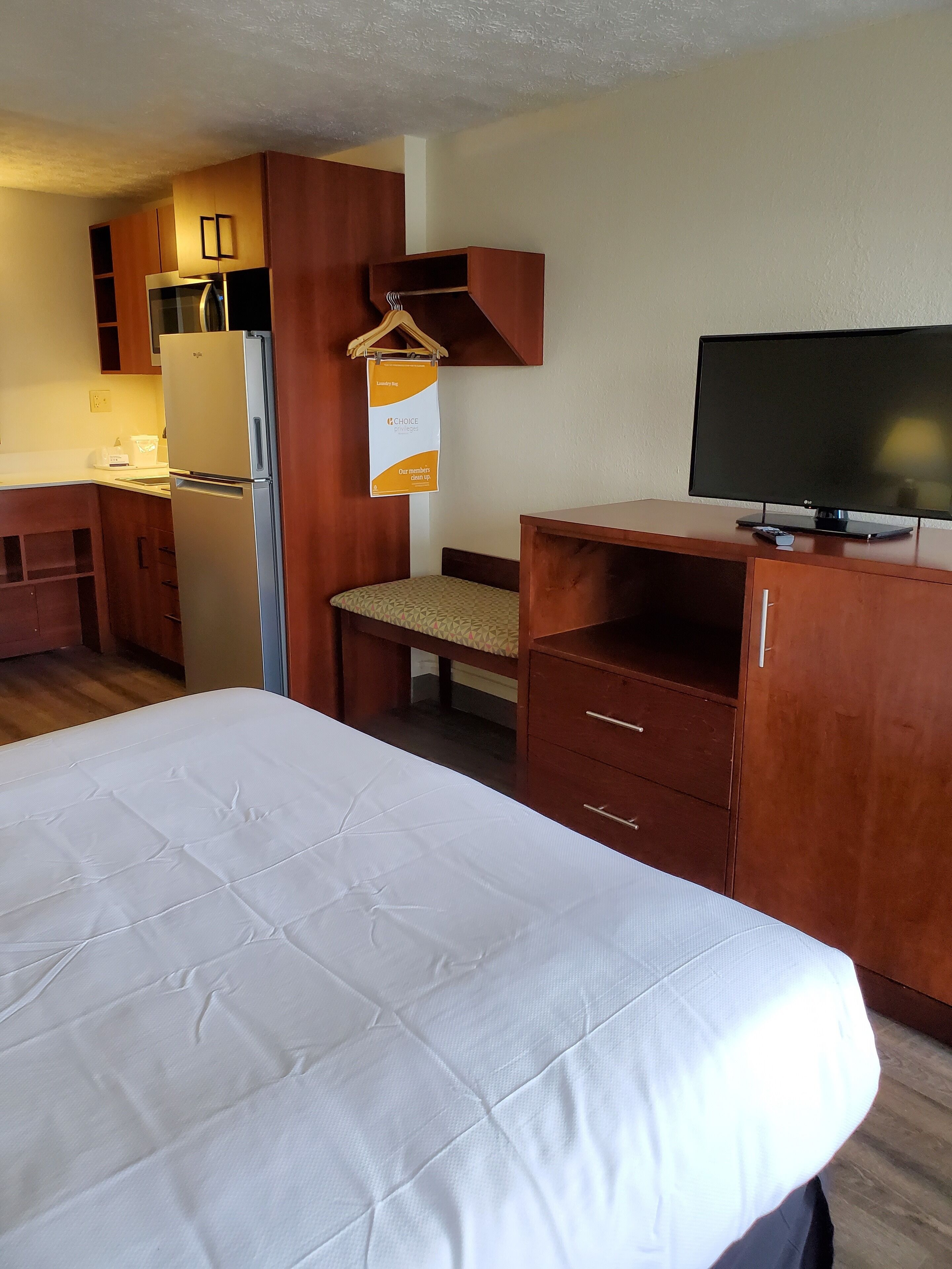 A hotel room with a bed, a desk, a television, a refrigerator, and a kitchen area.