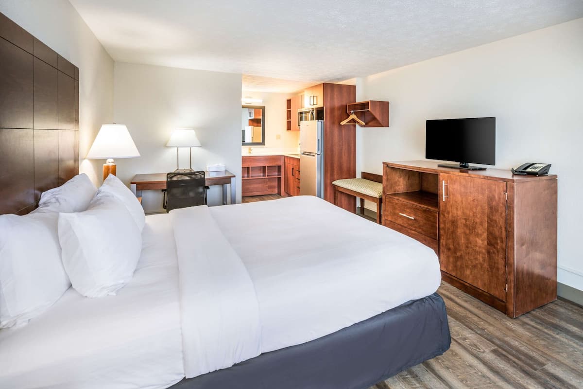 A hotel room with a large bed, a desk, a television, and a kitchenette.