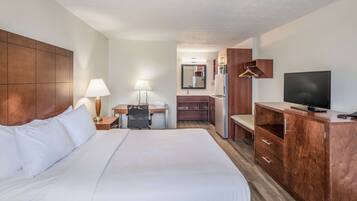 Quarto de hotel com uma cama grande, uma escrivaninha com cadeira, televisão, guarda-roupa e um espelho.