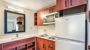 A modern kitchen with wooden cabinets, a white countertop, a built-in microwave, and a refrigerator. - Suburban Studios Middlesboro (Middlesboro)