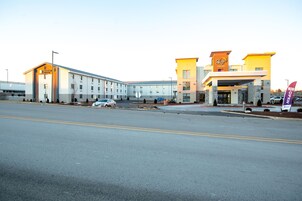 Un hotel moderno con entrada central, varios espacios de estacionamiento y cielo despejado.