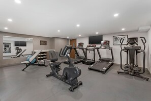Une salle de sport équipée de divers appareils, notamment des tapis de course, un vélo elliptique et un vélo d’appartement.