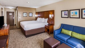 A hotel room with a large bed, a blue sofa, a wooden nightstand, and framed pictures on the wall. - Comfort Inn Charleston South (Charleston)