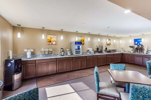 A hotel kitchen with a water dispenser, coffee maker, and a refrigerator. There are chairs and a table in the dining area.