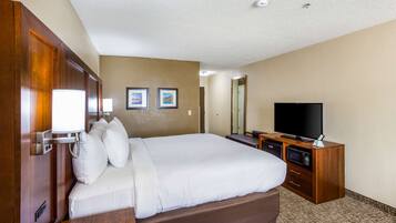 A hotel room with a large bed, a TV, a desk with a lamp, and a mirror on the wall.
