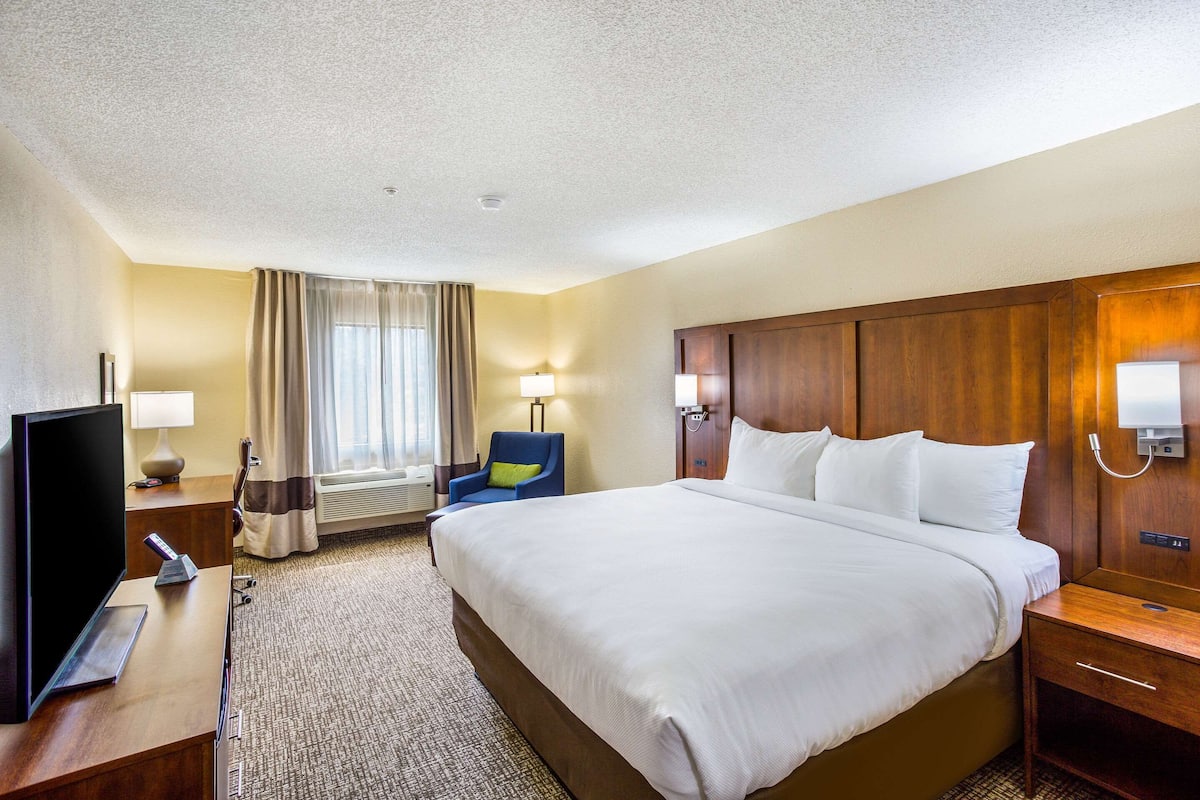 A hotel room with a large bed, a TV, a desk, a chair, and a window with curtains.