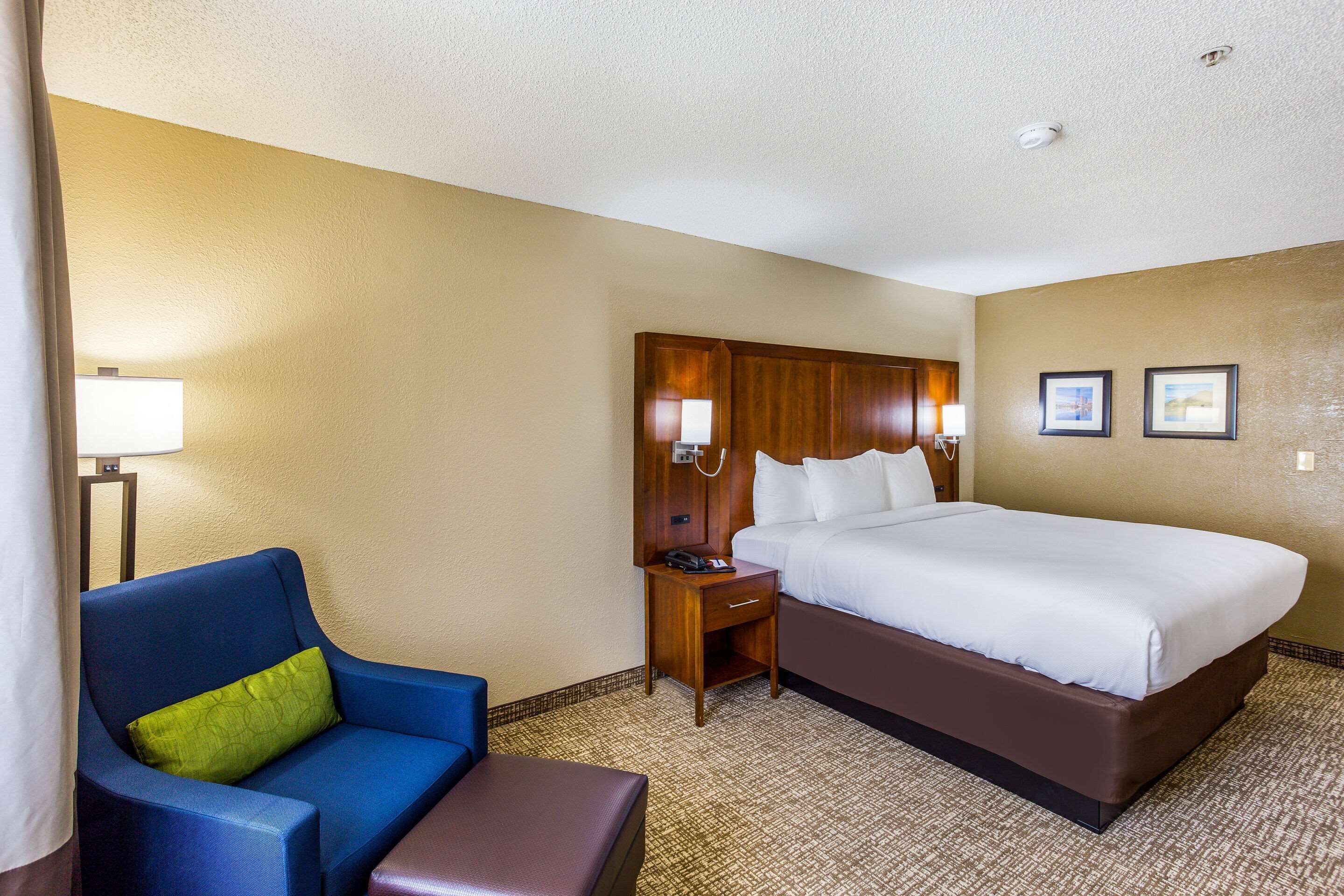 A hotel room with a large bed, a blue armchair, a small wooden nightstand, and a lamp.