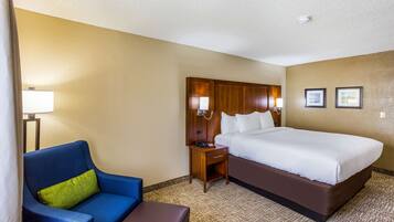 A hotel room with a large bed, a blue armchair, a small wooden nightstand, and a lamp.