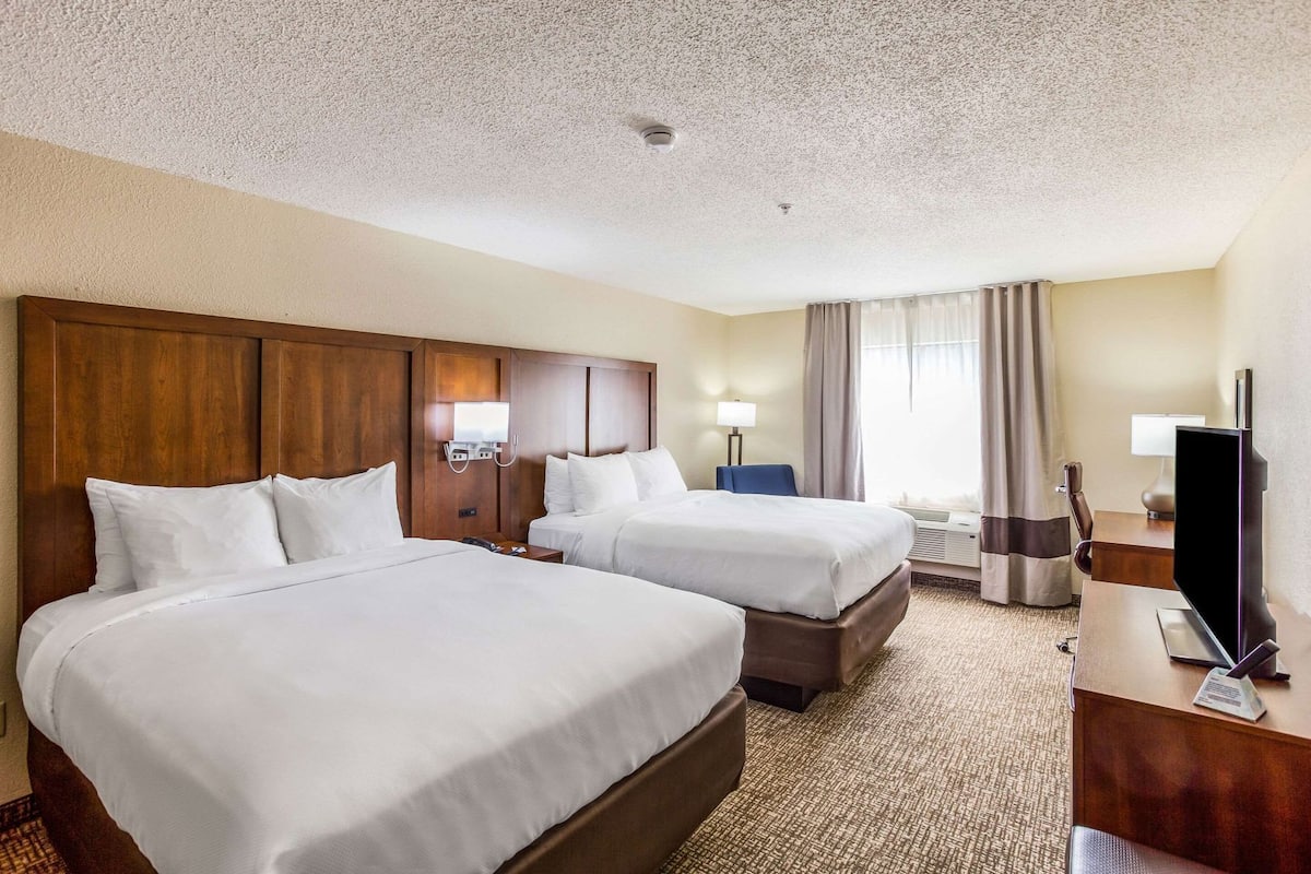 A hotel room with two beds, a desk, a TV, and a window with curtains.