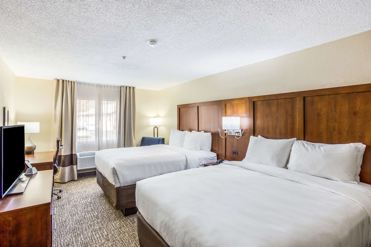 A hotel room with two beds, a desk with a TV, and a window with curtains.