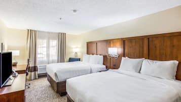 Una habitación de hotel con dos camas, un escritorio con televisor y una ventana con cortinas.