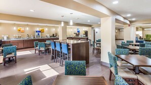 A hotel dining area with multiple tables and chairs, a central bar, and a kitchen area in the background. - Comfort Inn Charleston South (Charleston)