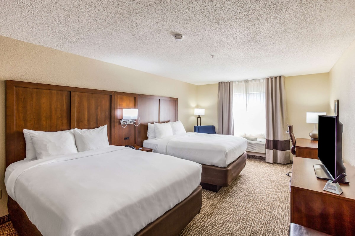 A hotel room with two beds, a desk, a TV, and a window with curtains.