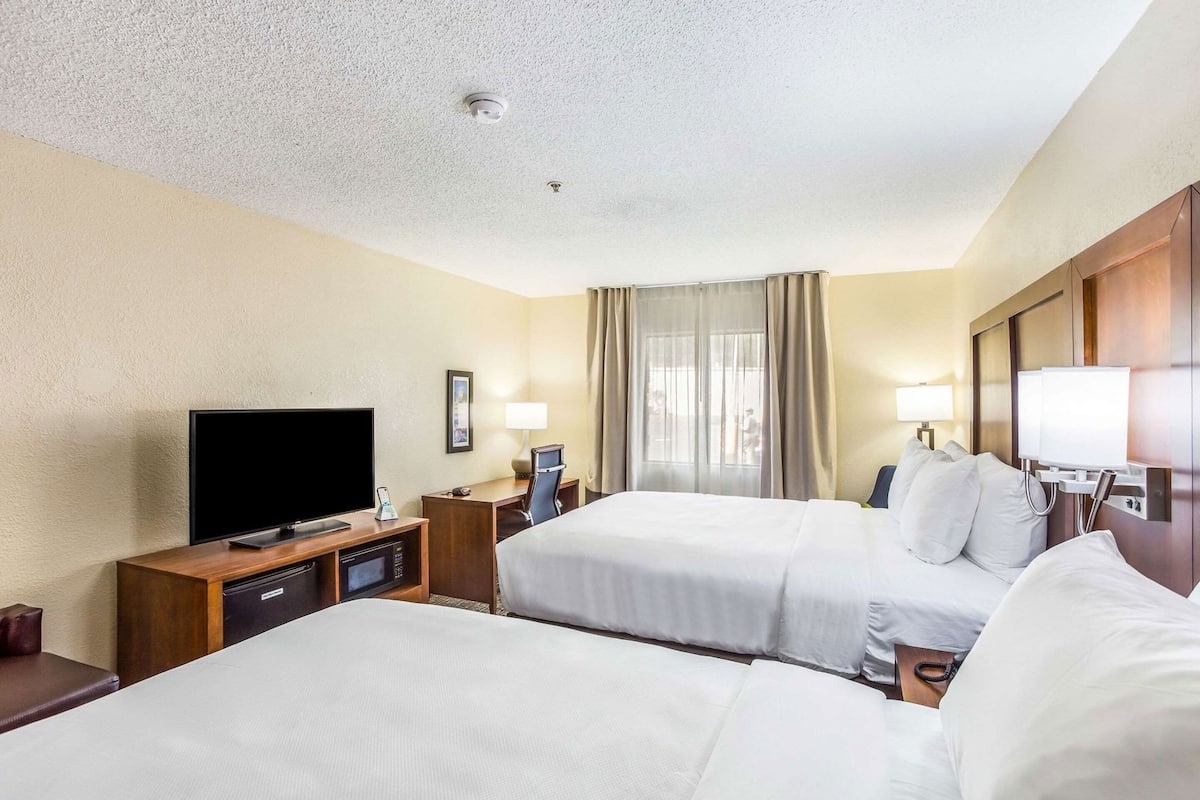 A hotel room with two beds, a TV, a desk with a phone, and a window with curtains.