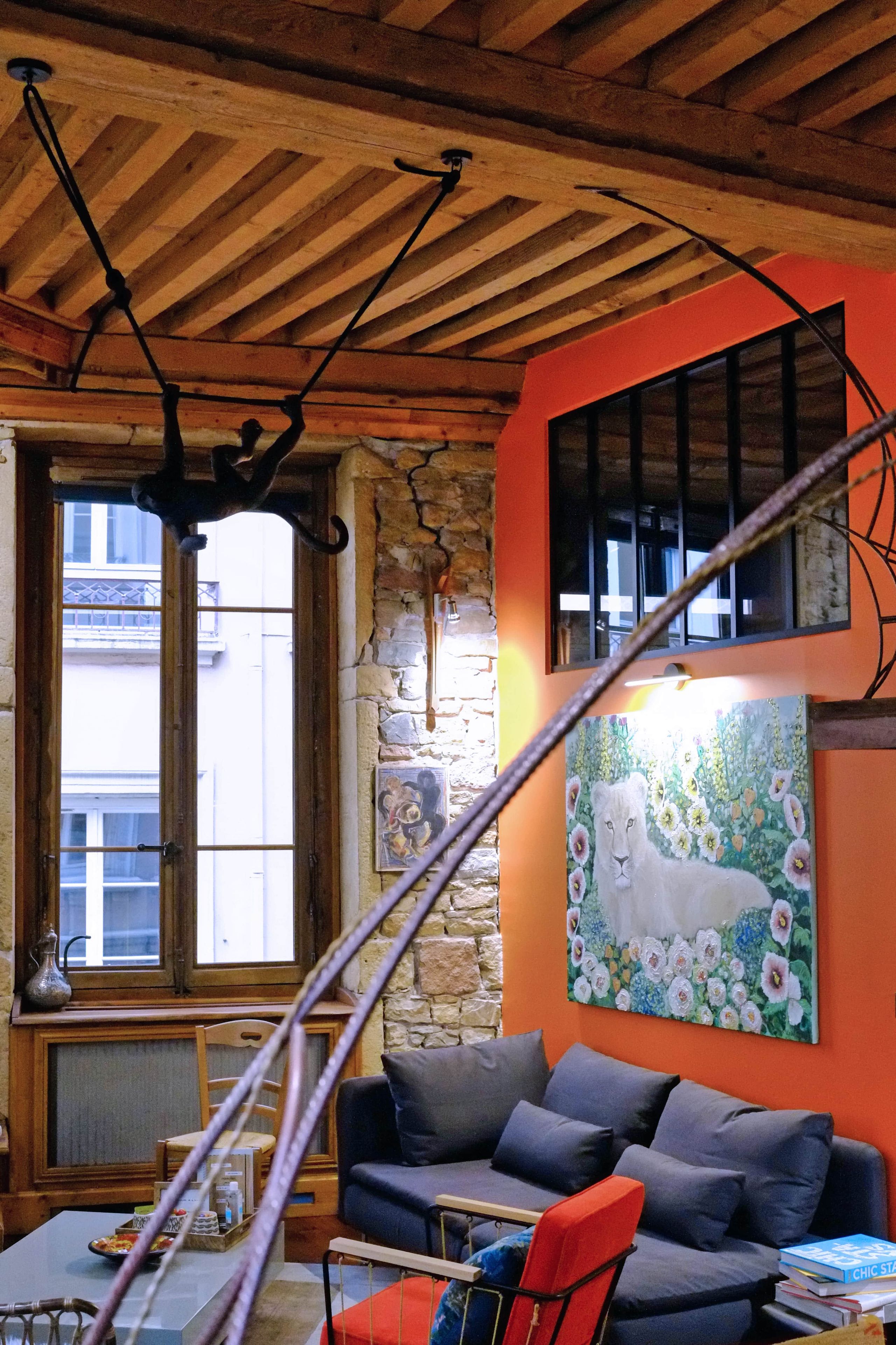 A room with a wooden ceiling, a stone wall, a window, a sofa, a chair, and a painting.