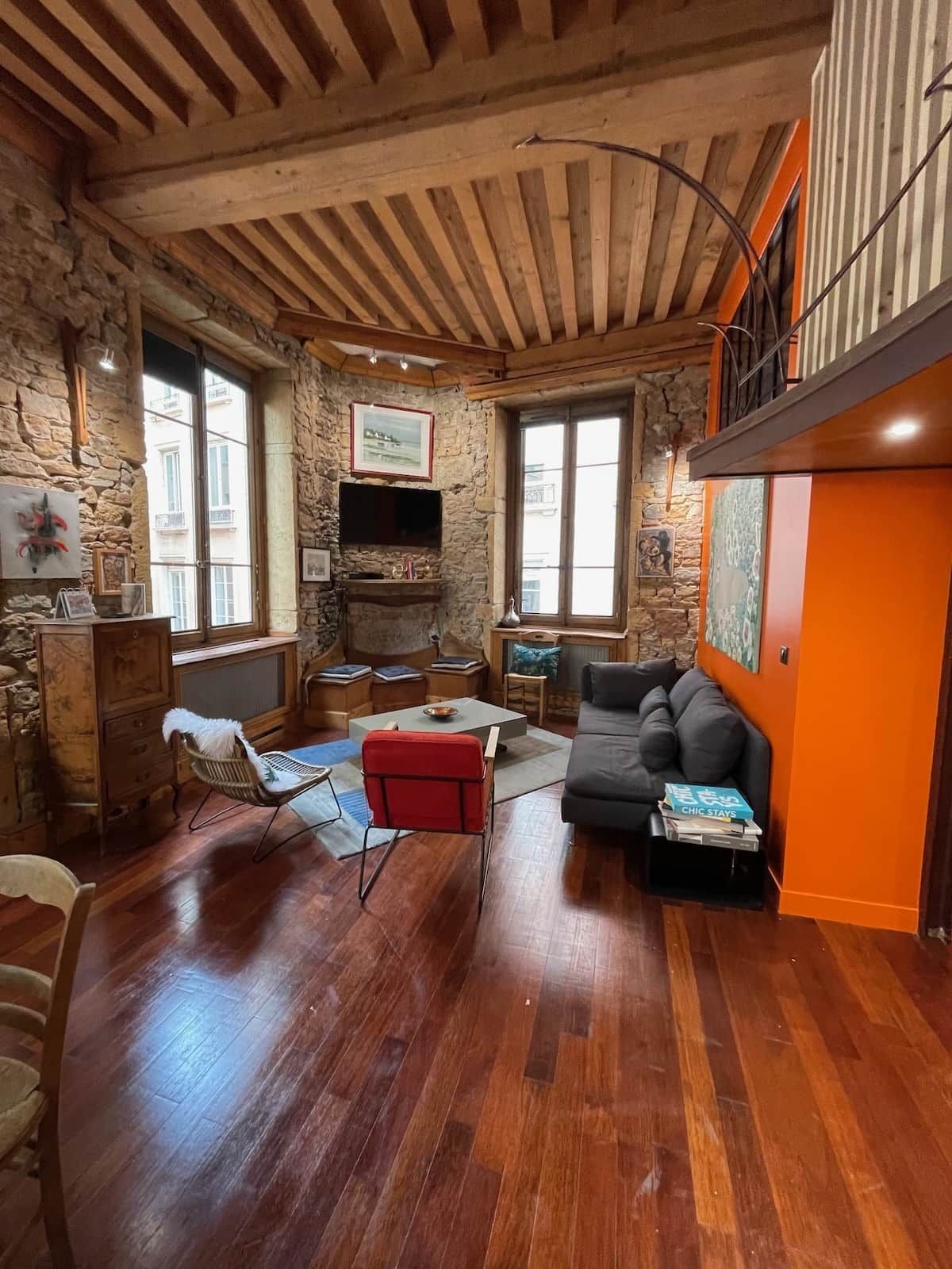 Un salon chaleureux avec un mur en pierre, des poutres apparentes en bois au plafond, un téléviseur à écran plat et un canapé.