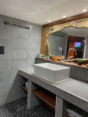 Une salle de bain moderne avec un lavabo blanc, un grand miroir doté d’un cadre décoratif et un sol carrelé.