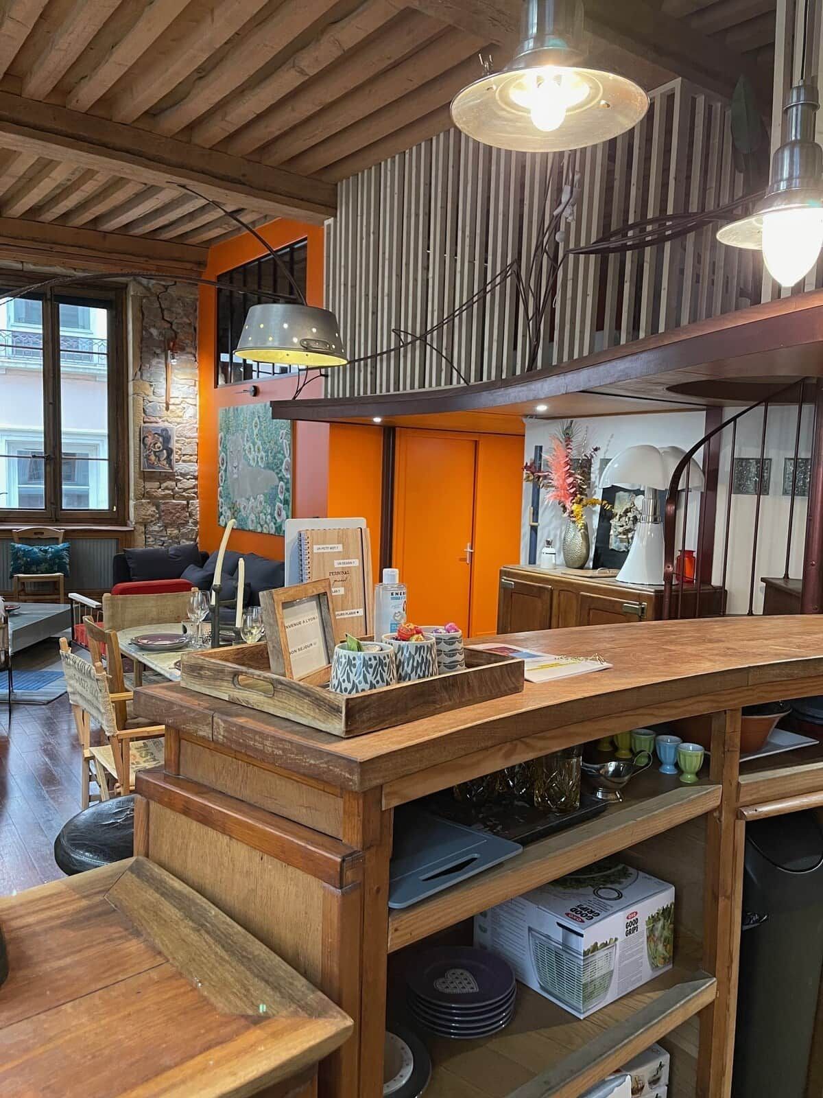 Une table à manger en bois avec un îlot central, entourée de chaises et d’un espace cuisine comprenant des placards et des appareils électroménagers.