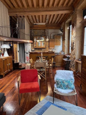 A rustic kitchen with wooden beams, a dining area with a red chair, and a bar area with a stone wall. - Charming "Heart of Lyon" Apartment with Elevator, A/C & Parking (Lyon)