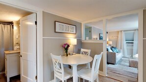 Un espace de vie compact comprenant un coin repas, une petite cuisine et un coin salon avec vue sur l’extérieur.