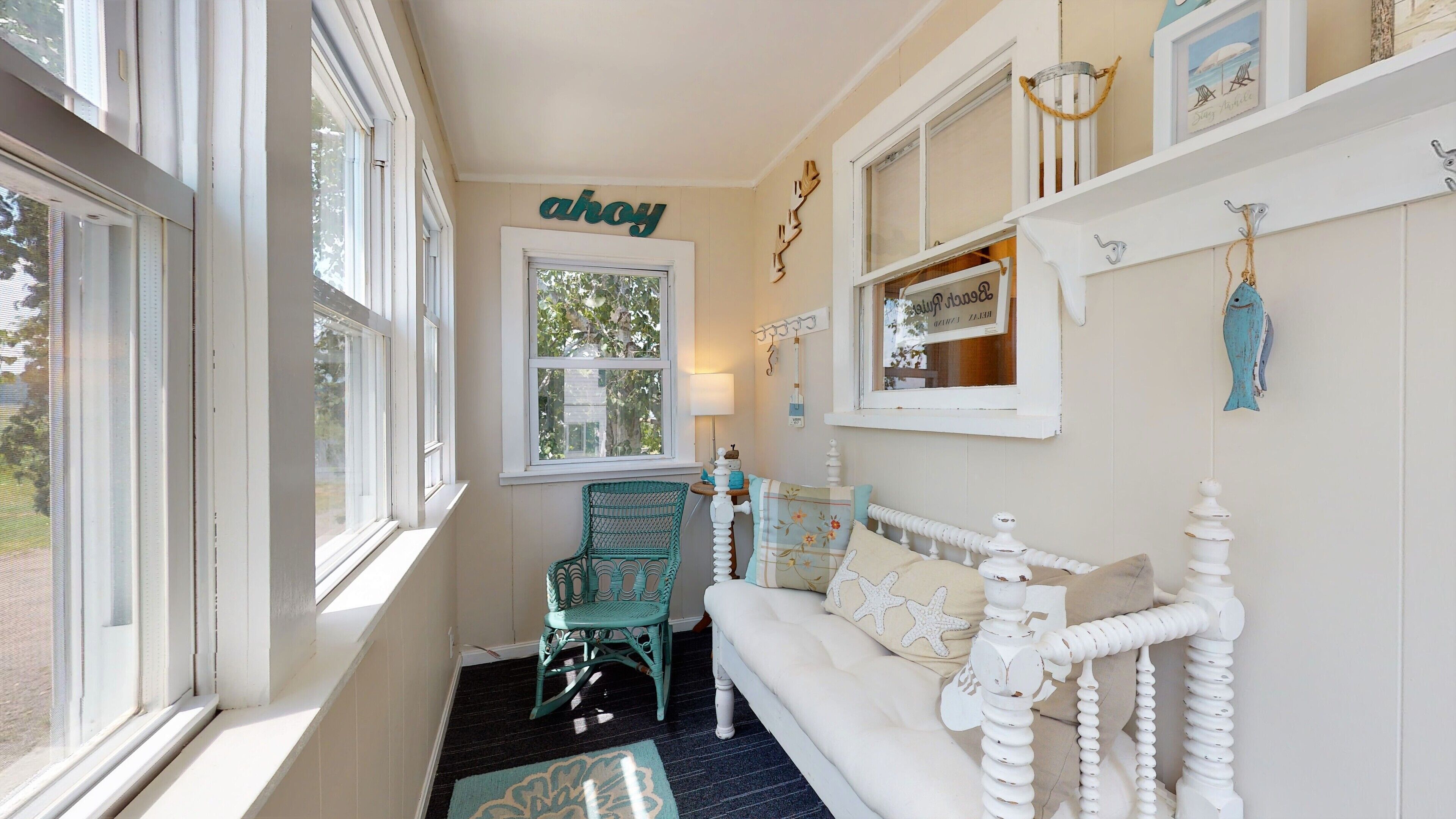 A narrow hallway with a white sofa, teal chair, and a window with 'ahoy' sign.
