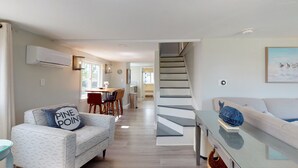 Un soggiorno moderno con un divano, una zona pranzo con tavolo e sedie, una scala e una cucina sullo sfondo.